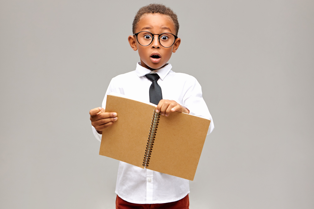<a href="https://www.freepik.com/free-photo/isolated-shot-emotional-shocked-african-pupil-wearing-white-shirt-black-tie-eyeglasses-having-surprised-astonished-look-keeping-mouth-widely-holding-open-blank-copybook-his-hands_11891296.htm">Image by karlyukav</a> on Freepik